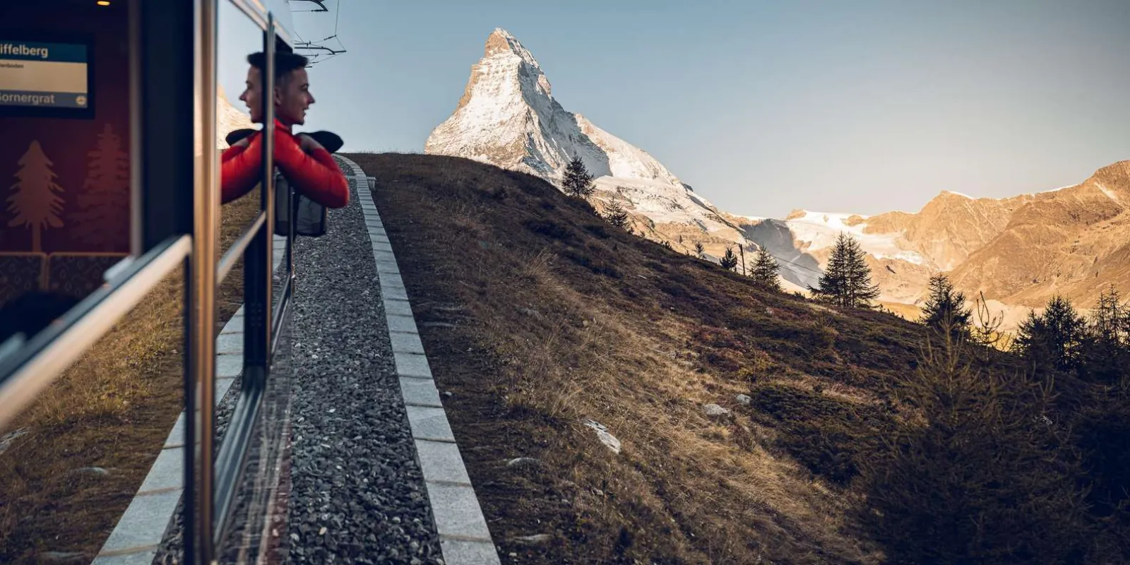 A passenger leaning from a Gornergrat train window with the Matterhorn ahead