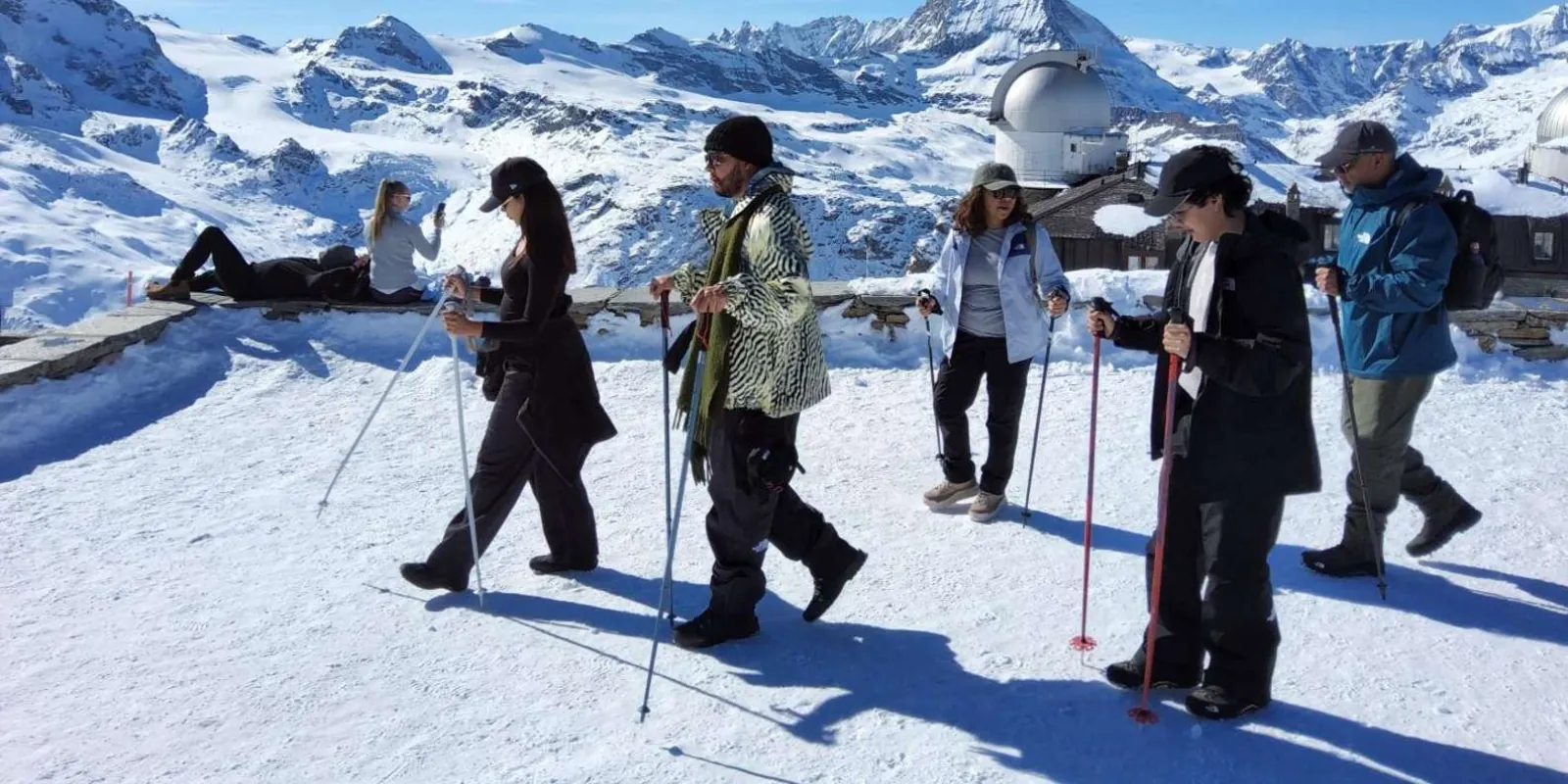 Walkers on the snow-covered Gornergrat ridge in winter with the observatory domes behind