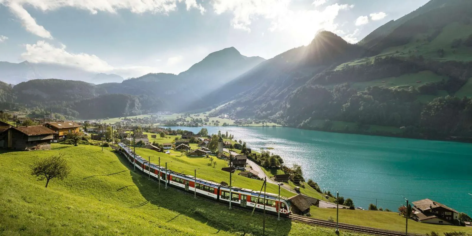 A Zentralbahn train running along the shore of turquoise Lake Lungern beneath green mountains