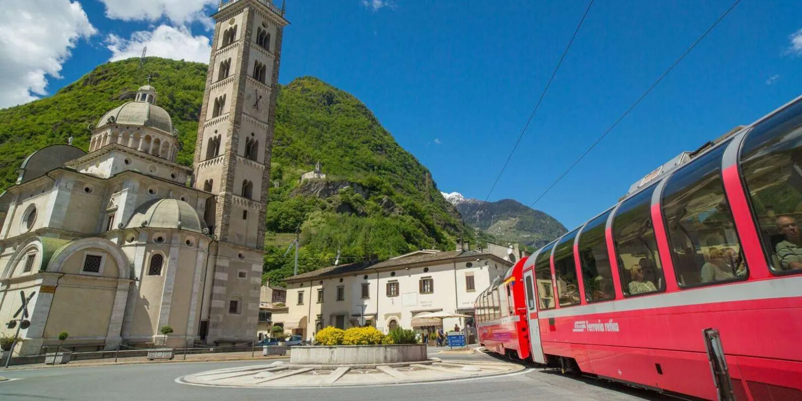 A red Rhaetian Railway train passing the domed basilica in the square at Tirano