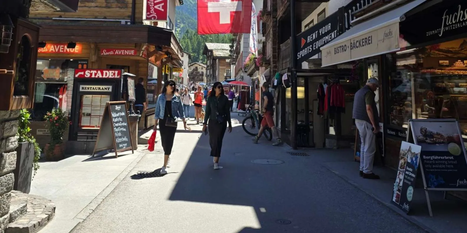 Shoppers on Zermatt's Bahnhofstrasse beneath a Swiss flag strung across the street