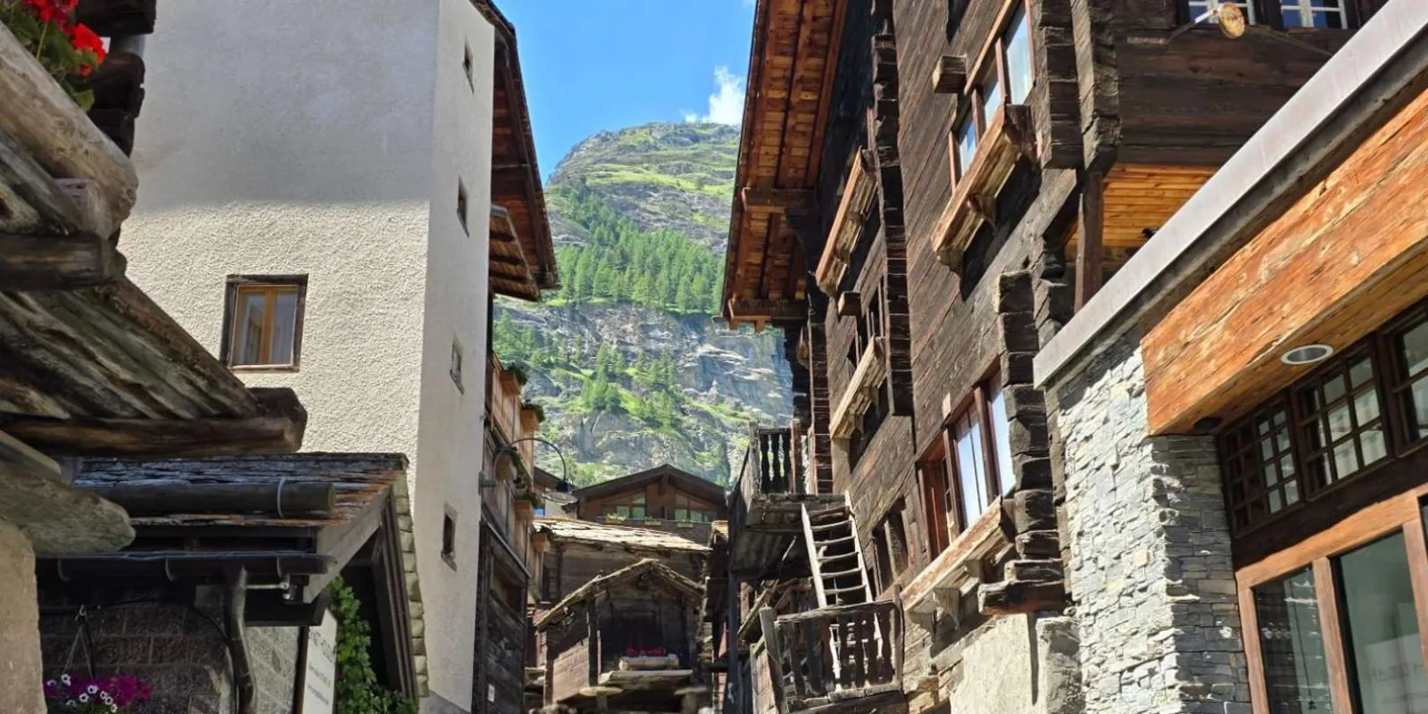 A narrow lane between weathered timber houses and geraniums in old Zermatt